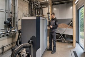 Technicien contrôlant une chaufferie collective à granulés avec silo en arrière-plan